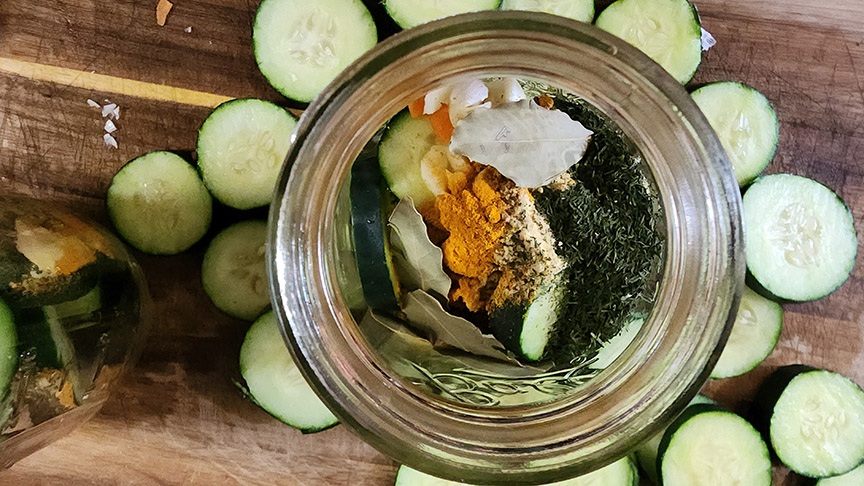 Cucumbers and spices in a canning jar on wooden table.
