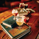 a flight of beer in small stemmed tulip glasses placed on classic library books