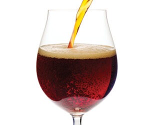 Dark ale or porter beer is pouring into snifter glass isolated on white background