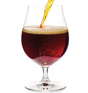 Dark ale or porter beer is pouring into snifter glass isolated on white background