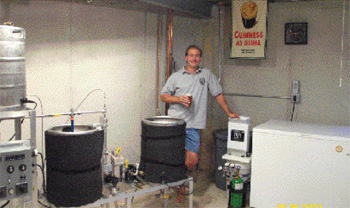 Man standing near his homebrewery equipment holding a glass of beer.
