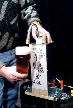 Hands operating a beer engine with a glass of beer.