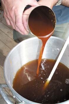 Hand pouring beer extract from a cup into a kettle.